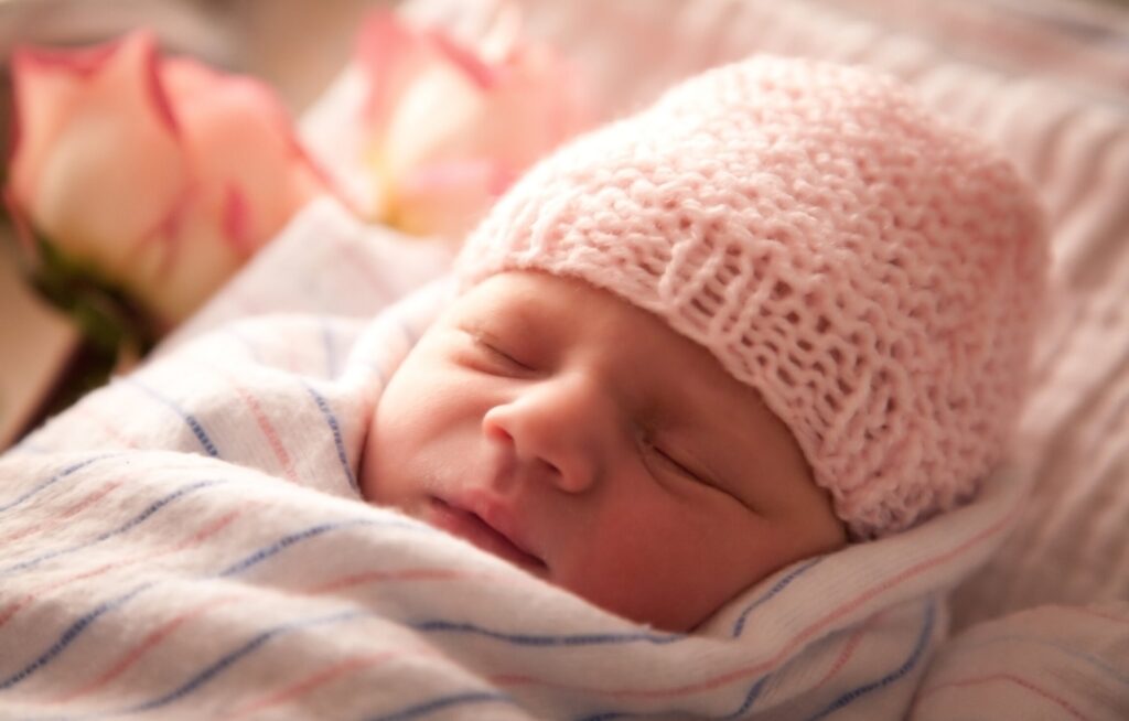 Bebê dormindo com gorro rosa e flores ao fundo