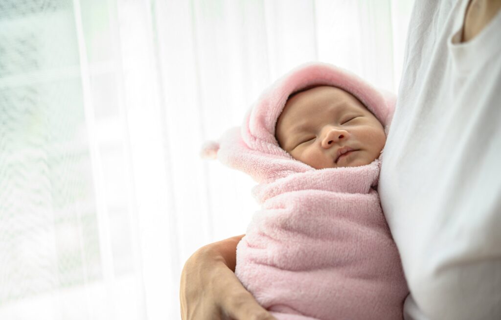 Bebê envolto em manta rosa, dormindo tranquilamente