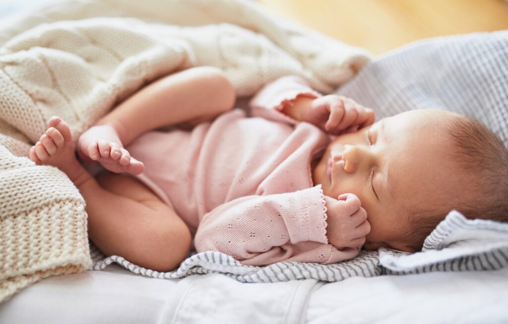 Bebê dormindo com gorro rosa e flores ao fundo