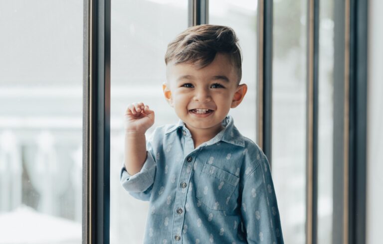 Criança sorrindo ao lado de uma janela