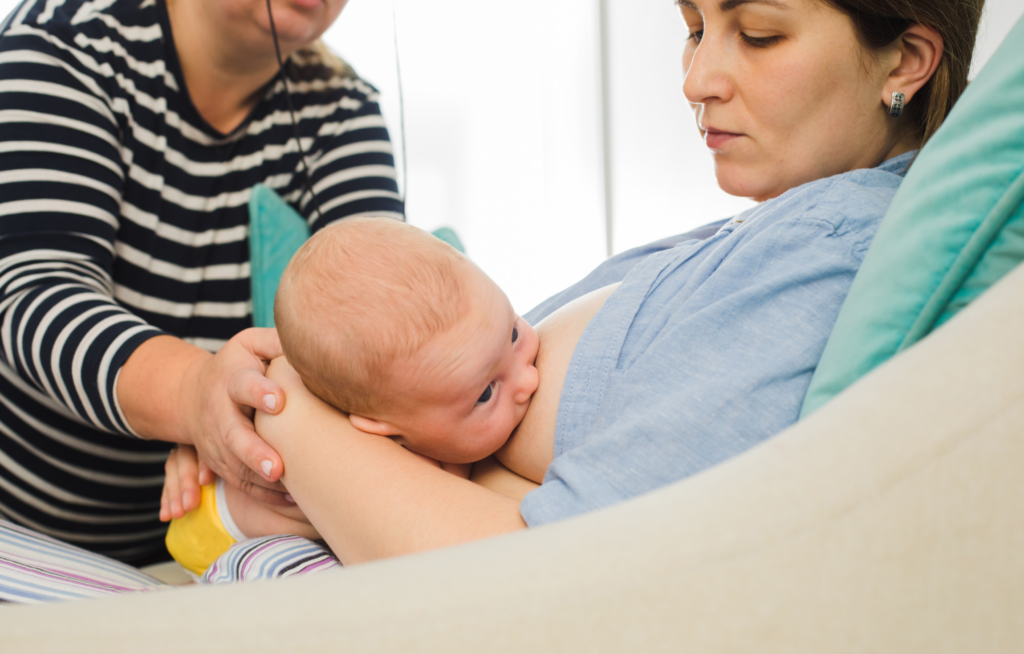 Mãe amamentando bebê com apoio de enfermeira.