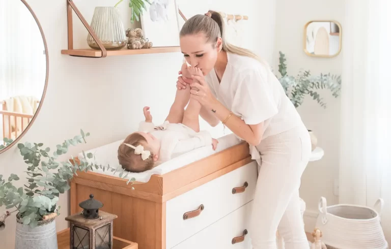 Mãe beijando pés de bebê no trocador de fraldas de madeira.