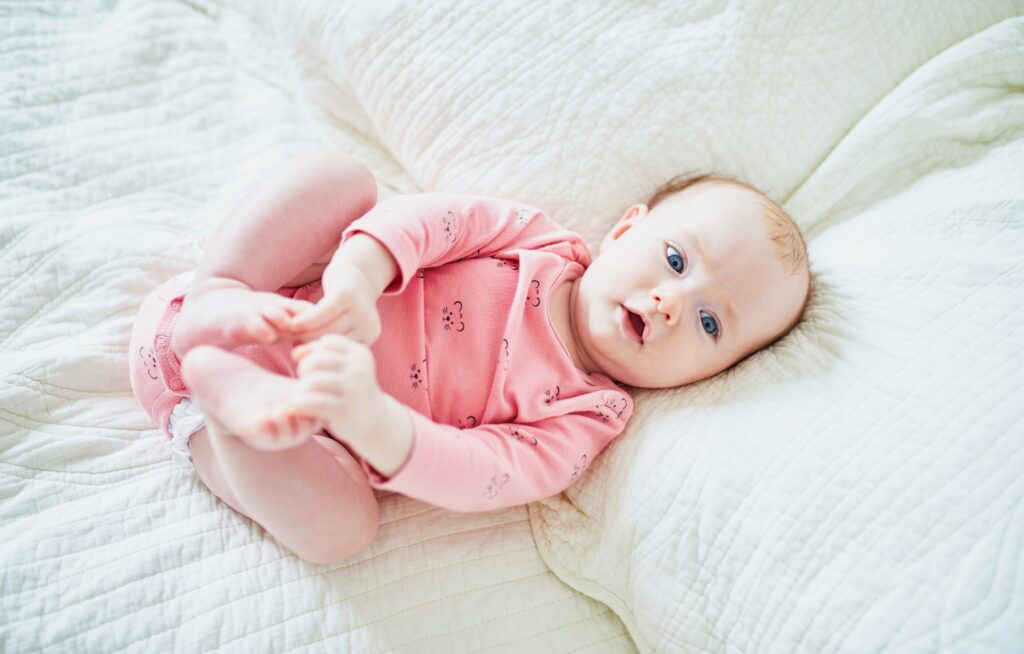 Bebê sorrindo em cama com lençol branco.