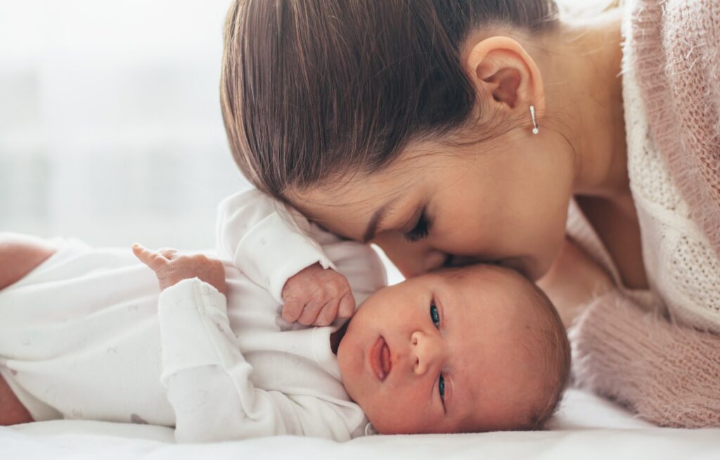 Mãe beija bebê recém-nascido em ambiente aconchegante