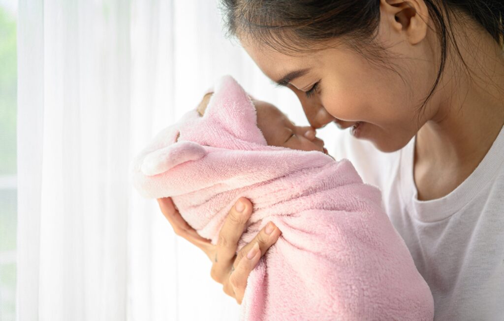 Mãe segurando bebê envolto em toalha rosa
