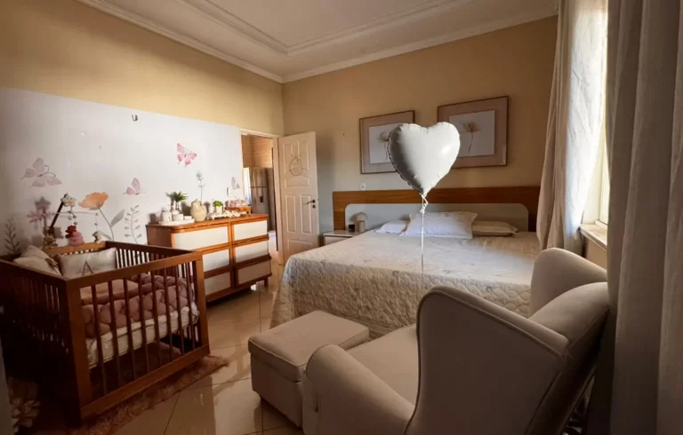 Quarto de casal com berço de madeira, poltrona de amamentação e decoração floral delicada."