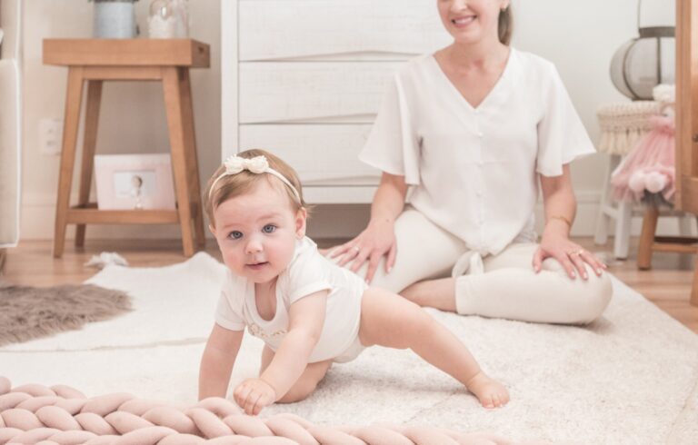 Bebê engatinhando em tapete com mãe ao fundo