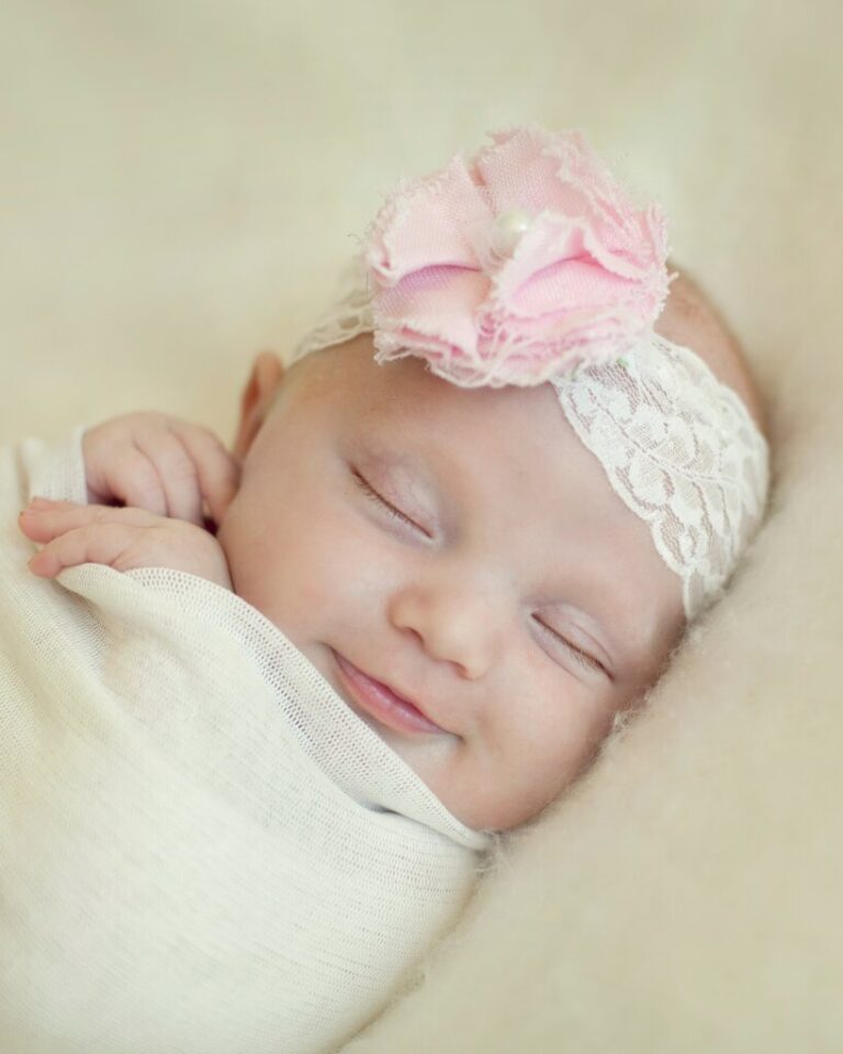 Bebê sorridente com laço rosa dormindo